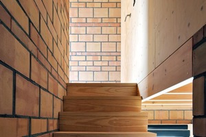  Links im Bild die bis unter das Dach aufsteigende tragende Ziegelwand, an der die Holztreppe in die oberen Geschosse führt 